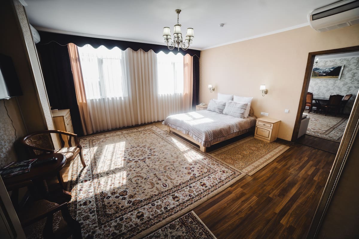 A bedroom with a bed, nightstands, a chair, a desk, a chandelier, and a large mirror.