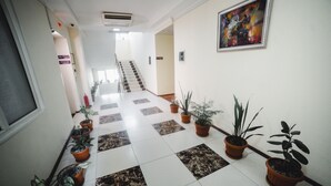 Un pasillo de hotel con piso a cuadros, plantas en macetas, una escalera y una obra de arte enmarcada en la pared.