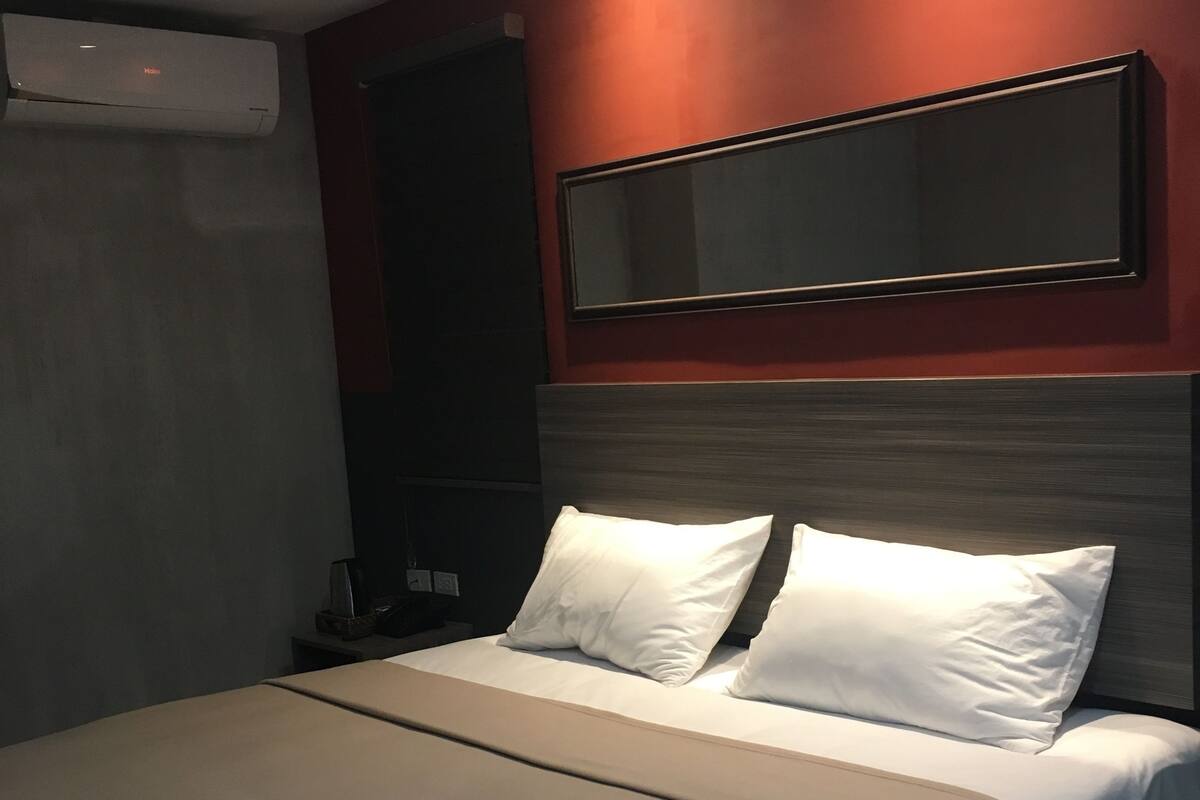 Ein modernes Hotelzimmer mit einem großen Bett, einem Flachbildfernseher, einem Nachttisch und einer Klimaanlage.