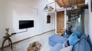 Una sala de estar moderna con un televisor de pantalla plana, un sofá azul, un taburete de madera y una escalera con barandilla de vidrio.