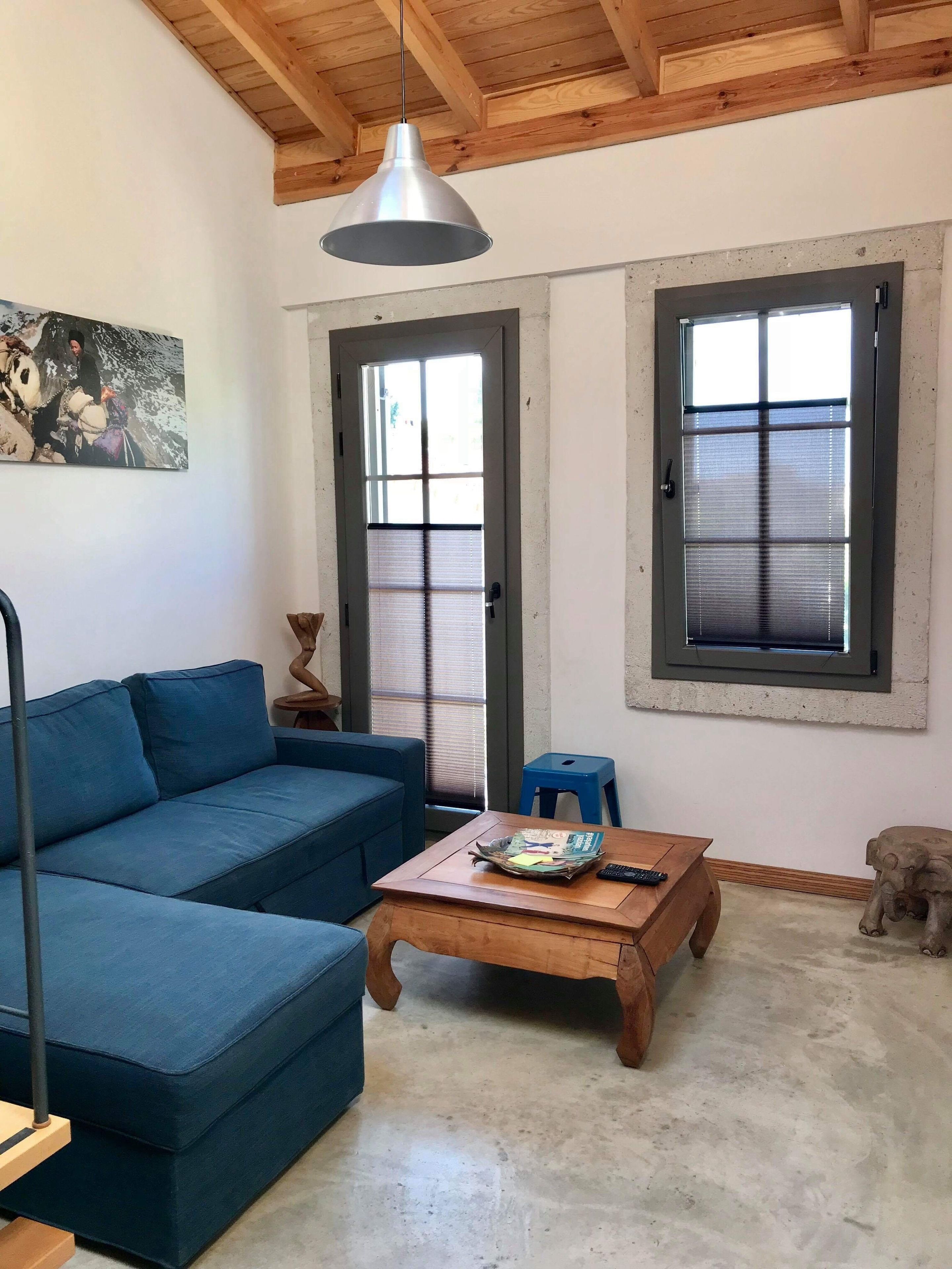Una sala de estar con un sofá azul, una mesa de centro de madera con revistas, una lámpara colgante y una puerta con ventana.