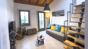 Una sala de estar con un sofá, una mesita, una escalera y un ventanal grande.
