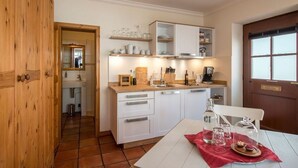Cocina compacta con armarios blancos, encimera de madera y comedor con mesa para dos.