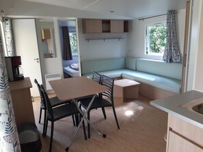 A compact living space with a kitchenette, a dining area, a built-in bench, and a window with curtains. - Relais du Haget (Cravenceres)