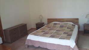 Un dormitorio con cabecera de madera, colcha acolchada, cómoda de madera y dos mesitas de noche con lámparas.