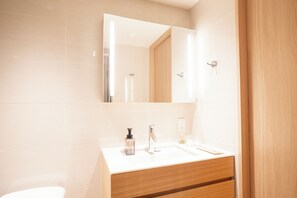 A modern bathroom with a white sink, mirror, and wooden vanity. - KABIN Koji (Kyoto)