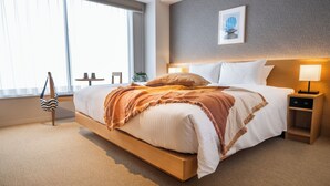 Et moderne hotelværelse med en stor seng, sengeborde, et vindue med rullegardiner og et billede i ramme på væggen.