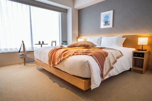 Ein modernes Hotelzimmer mit einem großen Bett, Nachttischen, einem Fenster mit Jalousien und einem gerahmten Bild an der Wand.