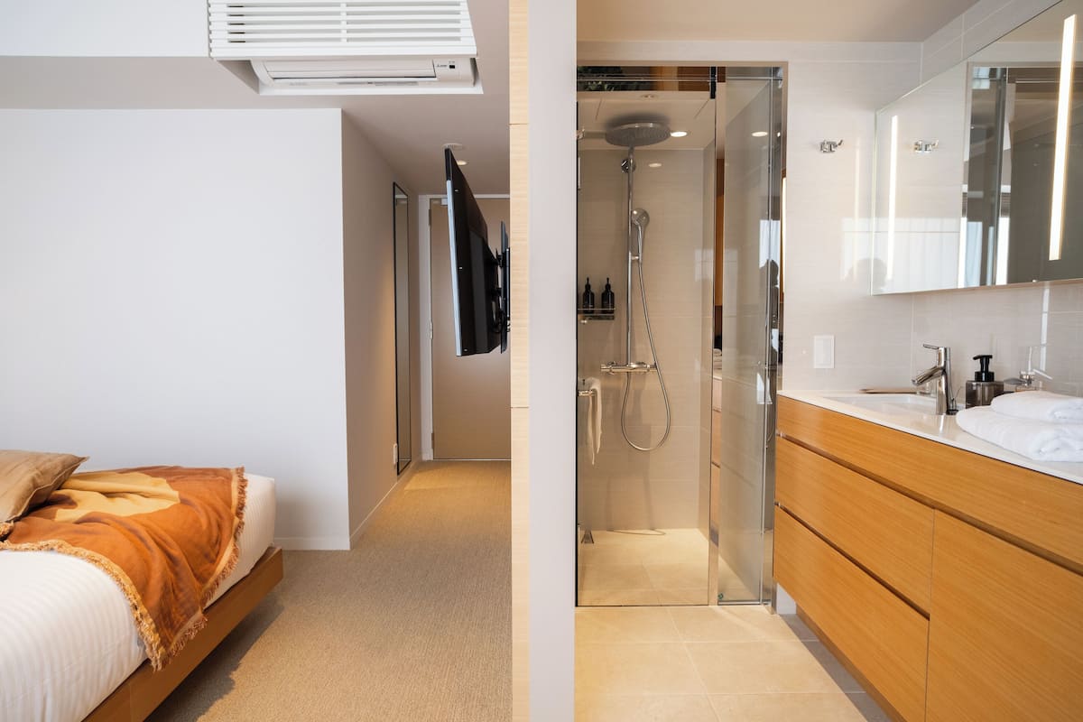 A bedroom with a bed, a bathroom with a shower, and a large mirror.