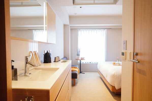 A modern hotel room with a large mirror, a double bed, a bedside table with a lamp, a small seating area, and a window with curtains. - KABIN Koji (Kyoto)