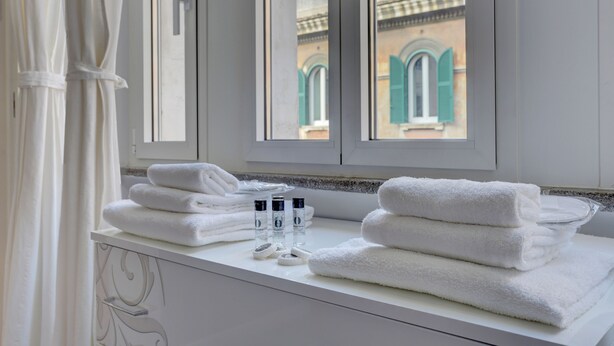 A bathroom with white towels stacked on a counter, a bottle of lotion, and a window with a view of buildings.