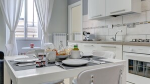 A modern kitchen with white cabinets, a dining table set with plates, cups, and utensils, and a window with curtains.