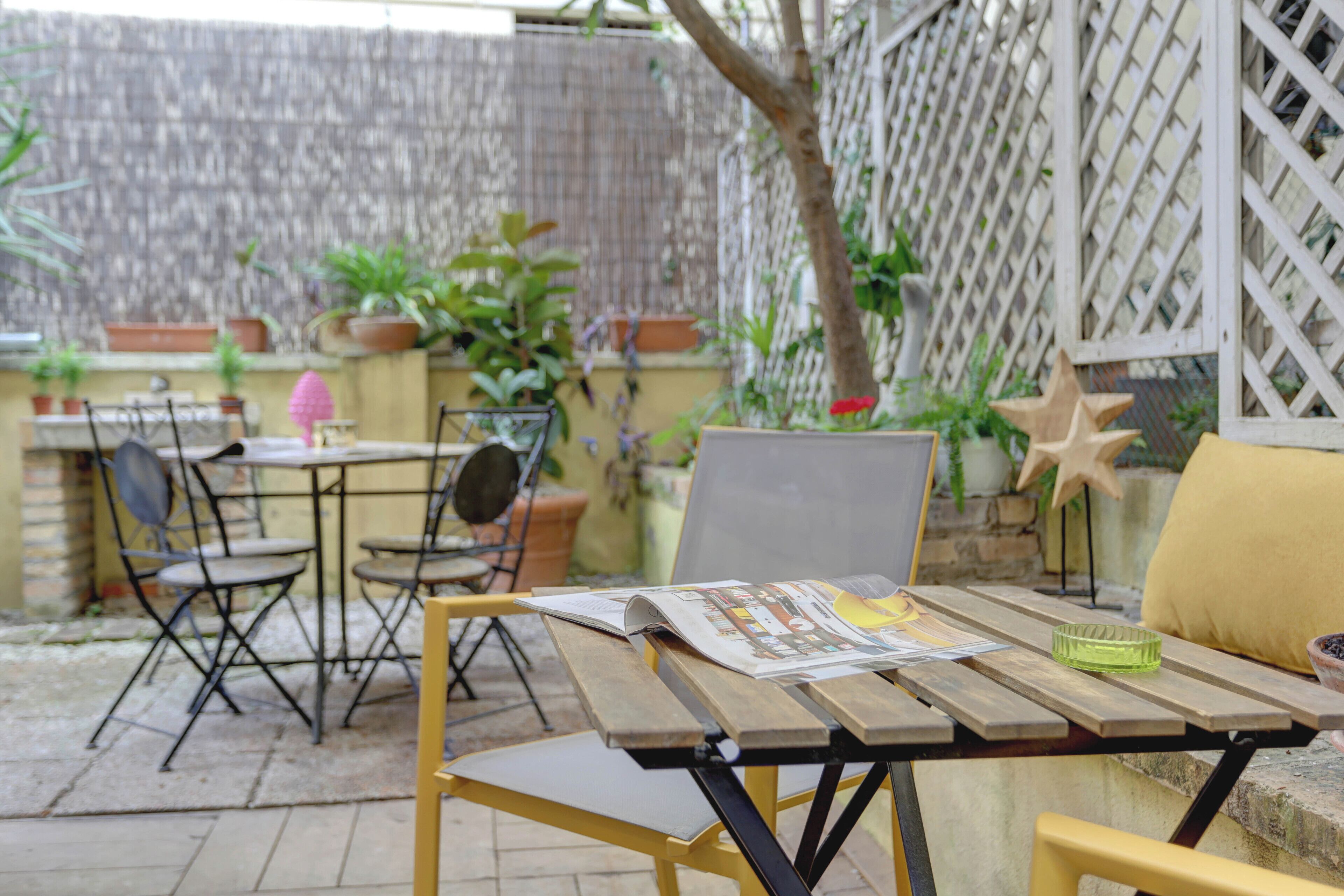 Una terrazza esterna con tavolo in legno, sedie in metallo e piante in vaso.