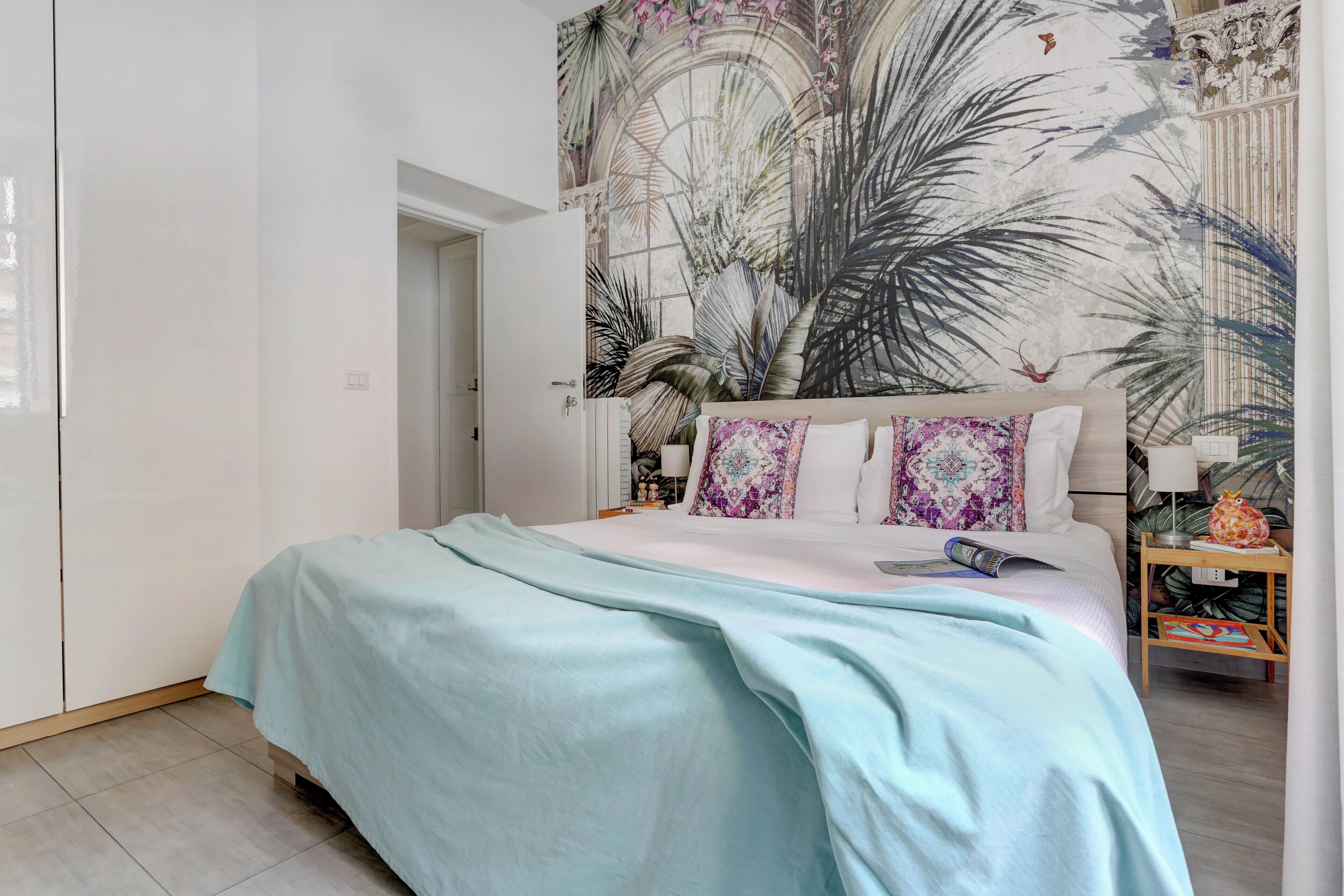 A bedroom with a bed, a nightstand, a wall mural, and a door.
