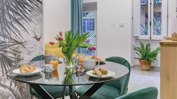 A dining area with a glass table, green chairs, breakfast items, and a view of the outside.