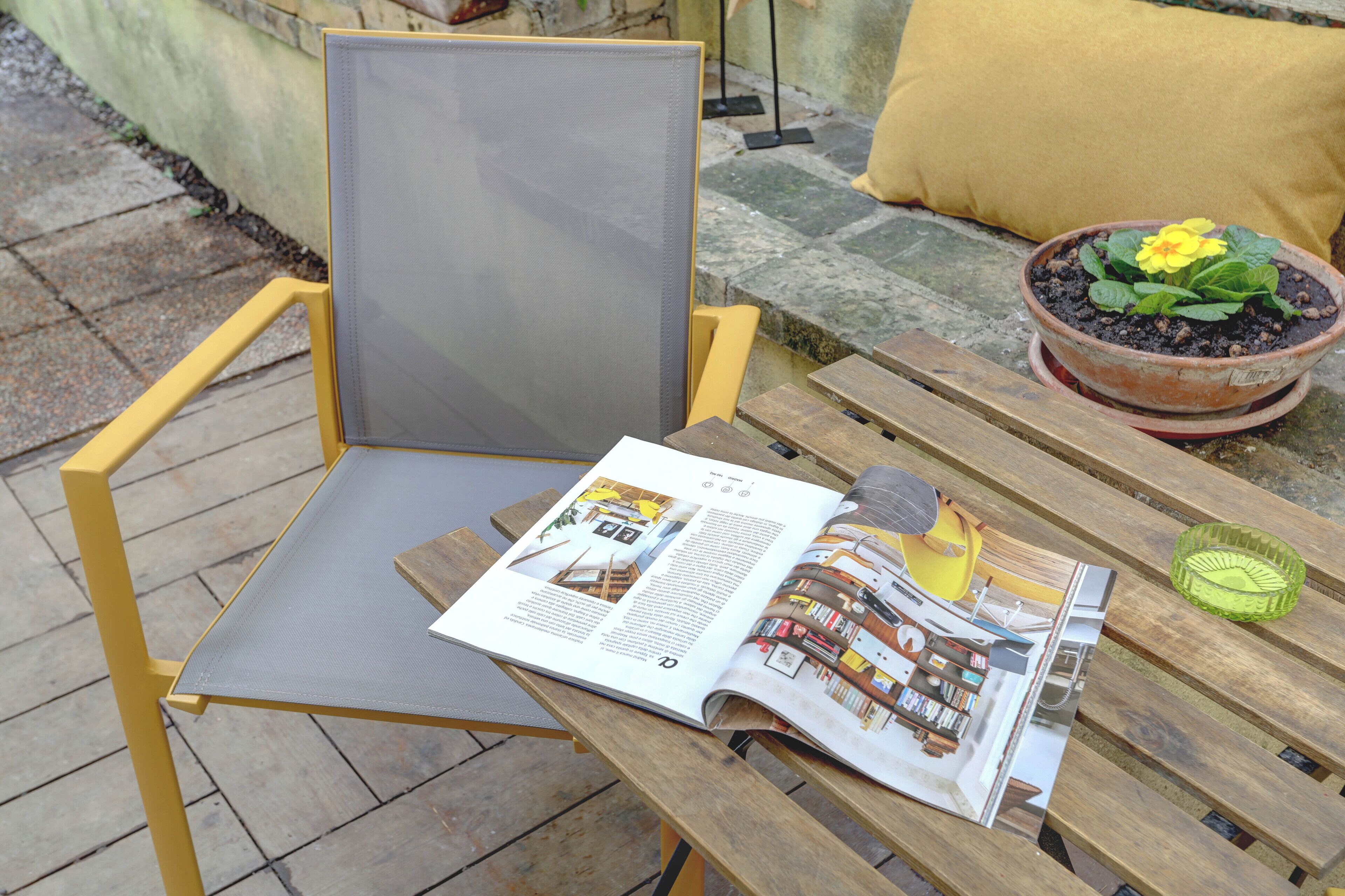 A magazine on a wooden table with a chair, a potted plant, and a cushion.