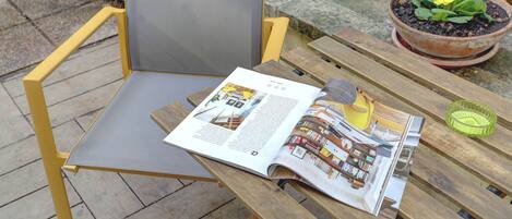 A magazine on a wooden table with a chair, a potted plant, and a cushion.