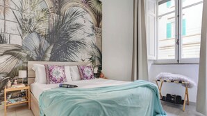 A bedroom with a bed, a nightstand, a window, and a wall mural.