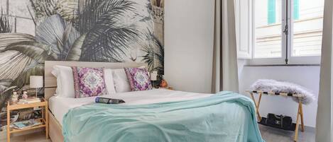 Un dormitorio con una cama, una mesita de noche, una ventana y un mural en la pared.