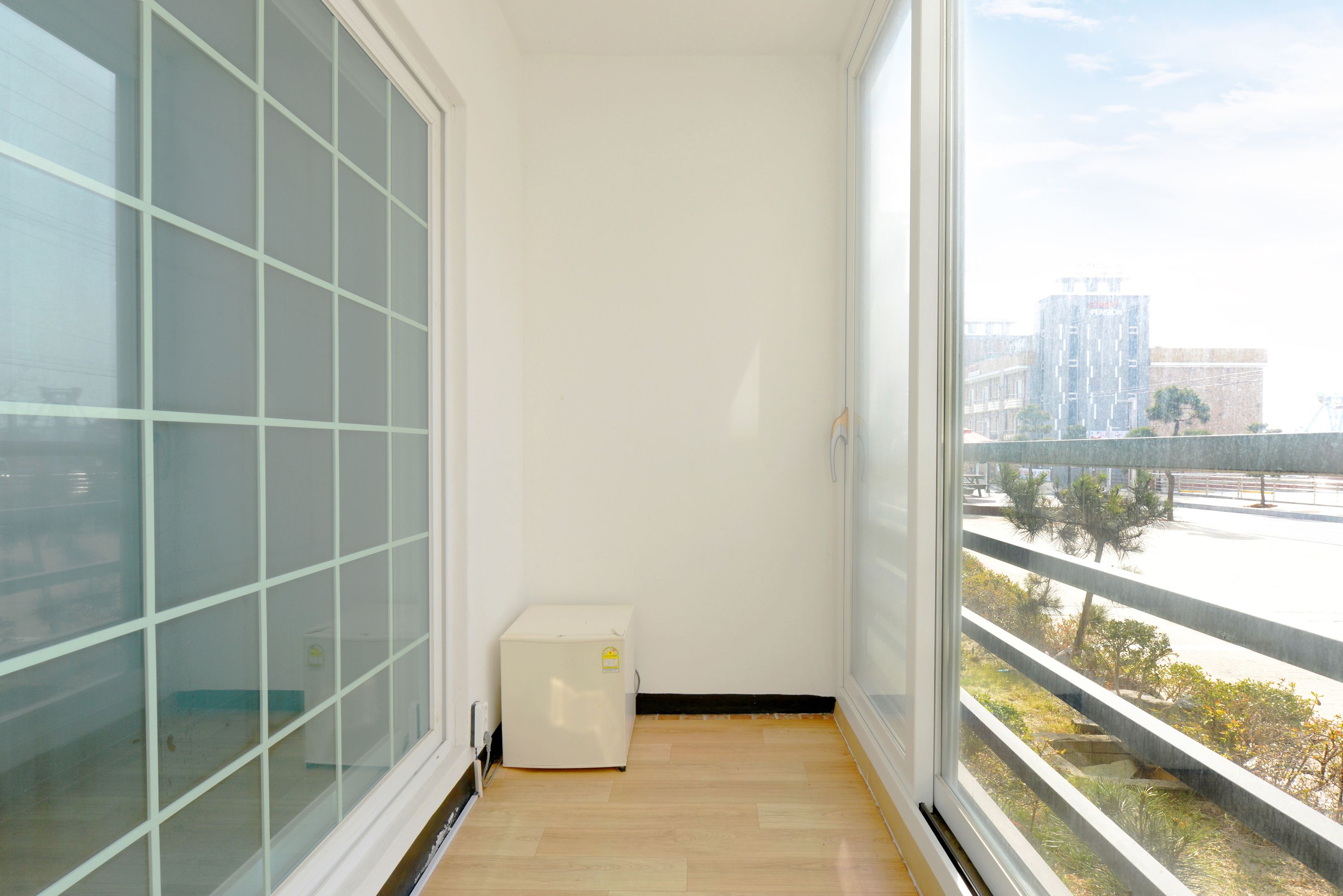 A narrow balcony with a view of a cityscape, a small white appliance, and a wooden floor.