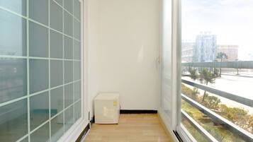 A narrow balcony with a view of a cityscape, a small white appliance, and a wooden floor.
