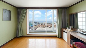 Una habitación con un ventanal grande, un escritorio con computadora y un mueble pequeño.