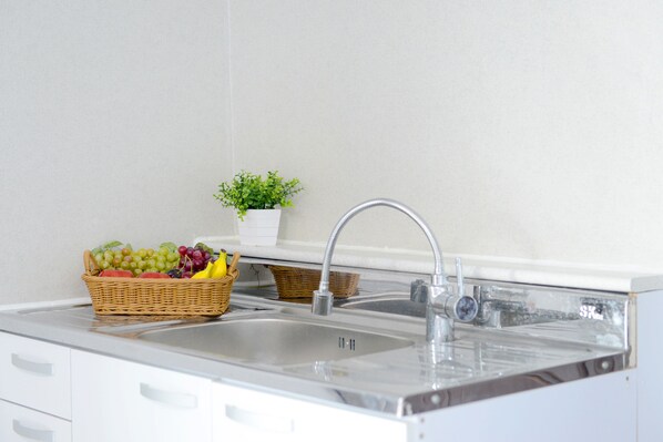 Une cuisine avec un évier en acier inoxydable, un panier en osier rempli de fruits et une petite plante en pot.