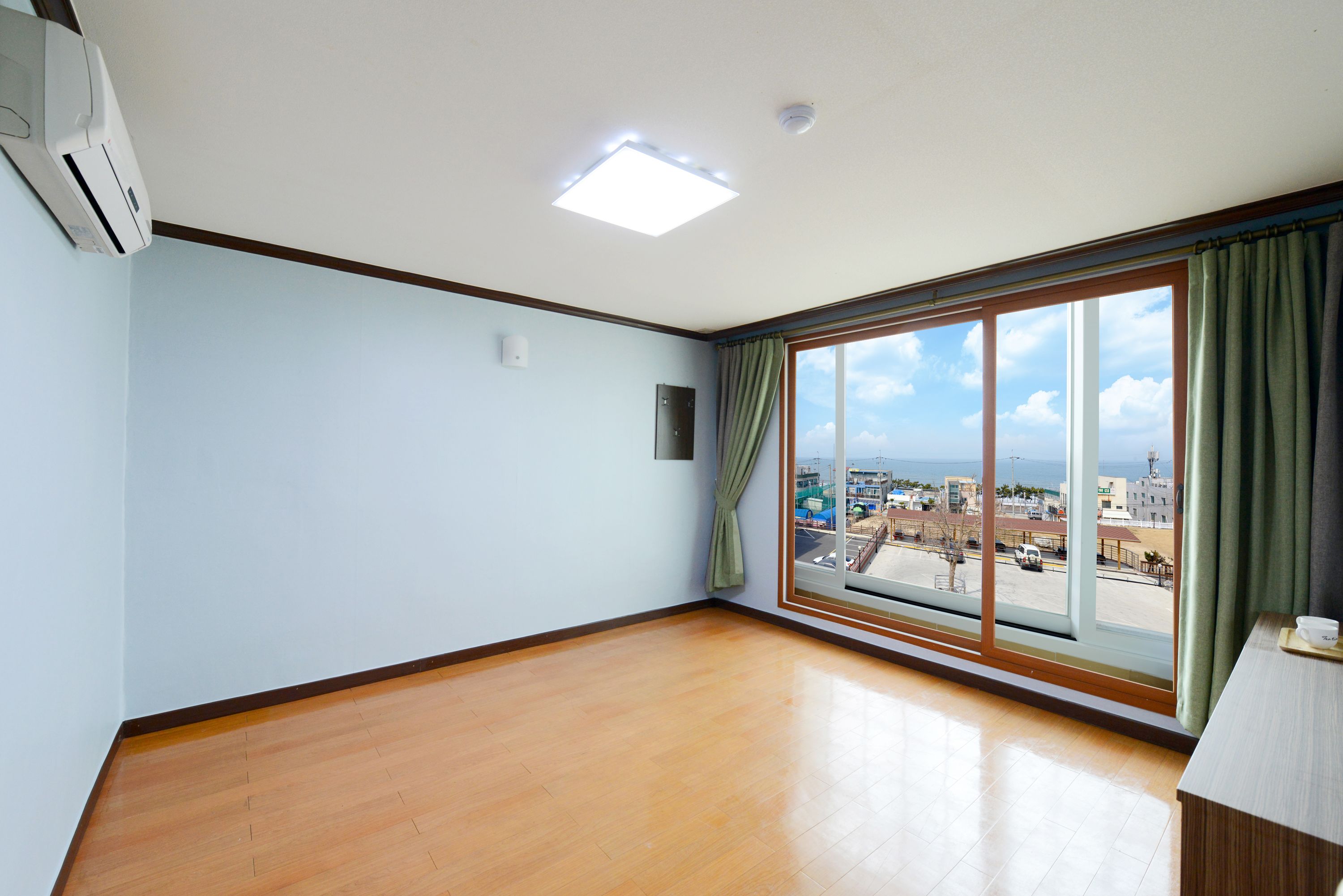 A room with a large window, wooden flooring, and a ceiling light.