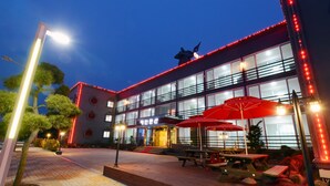 Un edificio moderno con fachada de vidrio, zona de estar al aire libre y luces rojas iluminadas.