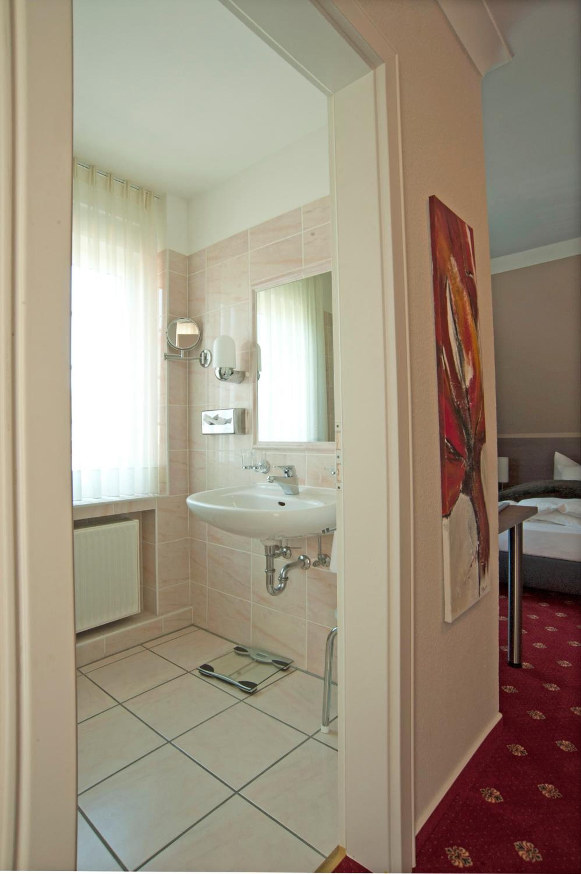 Un baño de hotel con un lavamanos blanco, un espejo y un cuadro floral rojo en la pared.