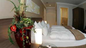 A hotel room with a bed, a bedside table with a vase of flowers, a lamp, and a painting on the wall. - Isselhorster Landhaus (Guetersloh)