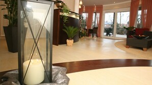 A reception area with a glass partition, a lit candle, potted plants, and a seating area with a sofa and chairs. - Isselhorster Landhaus (Guetersloh)