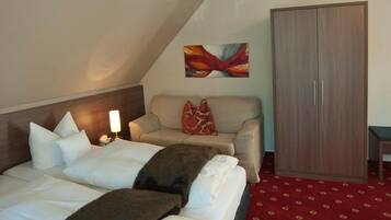 A hotel room with a bed, a sofa, a wardrobe, and a painting on the wall.