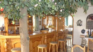 A bar area with wooden stools, a bar counter, and a decorative tree with hanging ornaments. - Isselhorster Landhaus (Guetersloh)