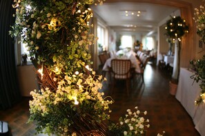 A restaurant interior with a long table and chairs, decorated with greenery and white flowers. - Isselhorster Landhaus (Guetersloh)