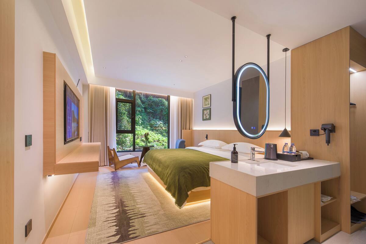 Un dormitorio moderno con una cama grande, una mesita de noche, un espejo y vistas al verde exterior.