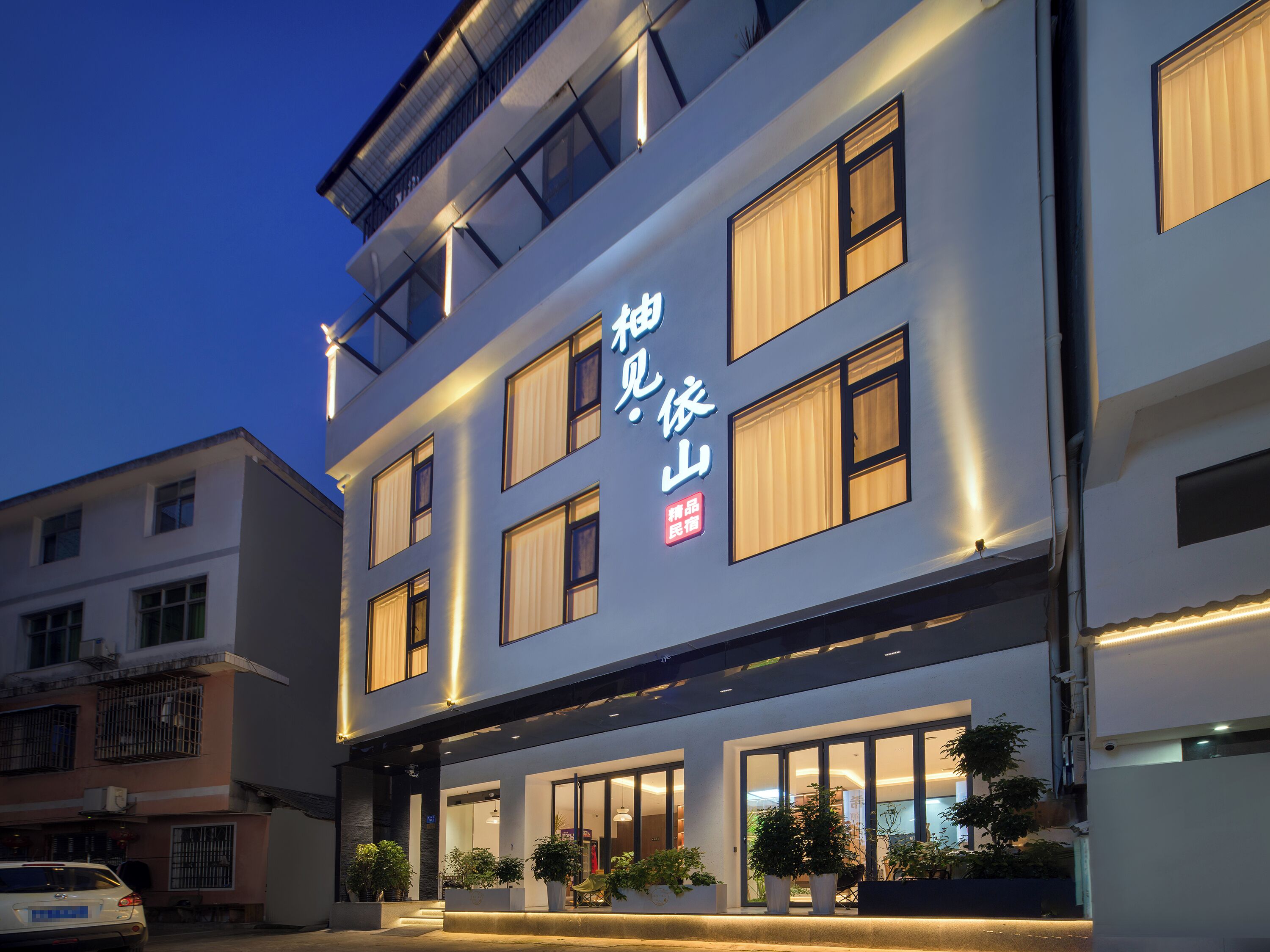 Ein mehrstöckiges Hotel mit beleuchteter Beschilderung, großen Fenstern und Topfpflanzen im Eingangsbereich.