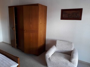 Una habitación con un armario de madera, un sillón blanco y una obra de arte enmarcada en la pared.