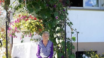 Een vrouw zittend op een bankje onder een overdekte structuur met bloemen.
