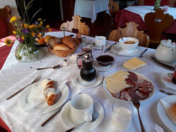 A breakfast table with bread, pastries, cheese, ham, and a coffee pot.