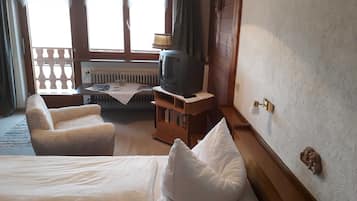 A hotel room with a bed, two armchairs, a small table with a lamp, a television, and a window with curtains.