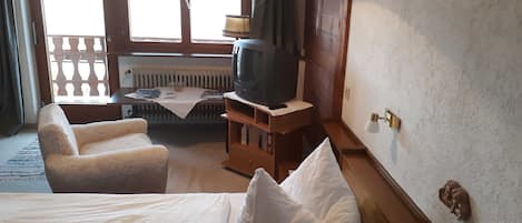 Habitación de hotel con cama, dos sillones, una mesita de noche con lámpara, televisor y ventana con cortinas.