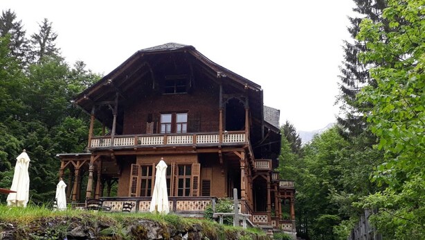 Une grande maison en bois dotée d’un balcon, entourée de verdure.