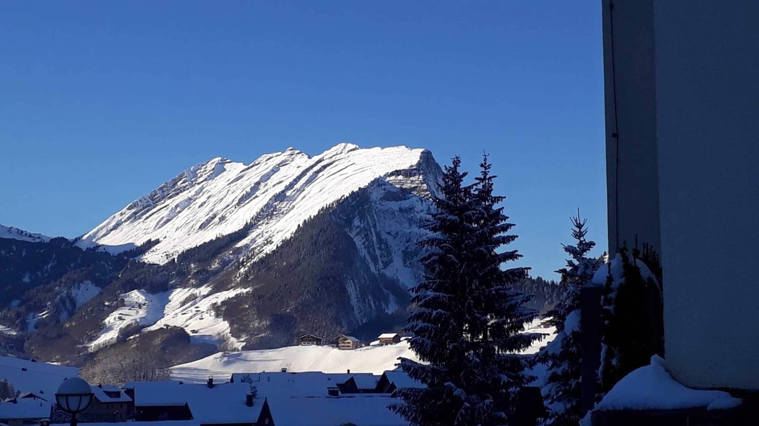 Een berg met besneeuwde toppen, een heldere lucht en enkele gebouwen aan de voet.