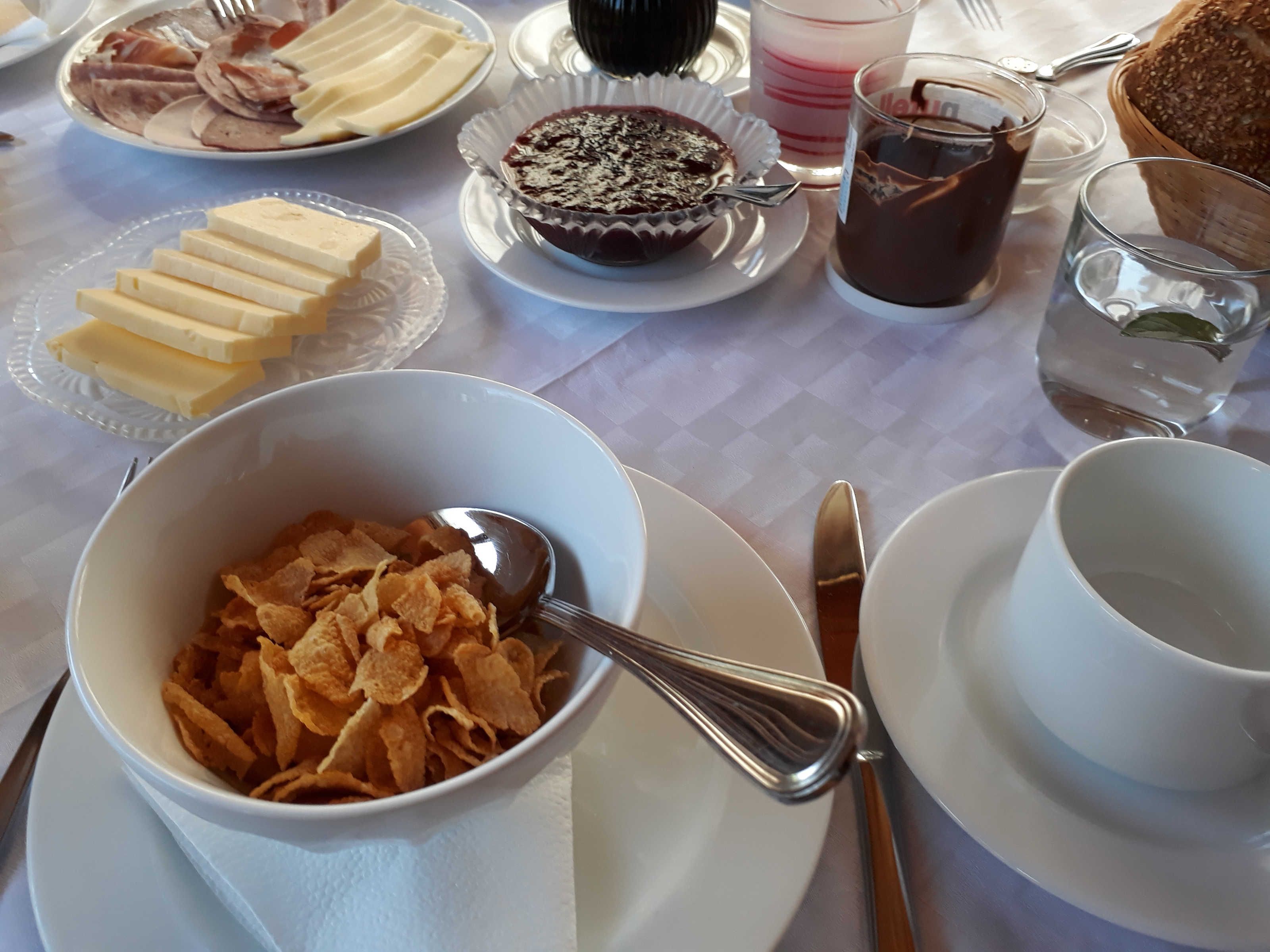 A breakfast table with cereal, butter, a muffin, a glass of juice, and a cup of coffee.
