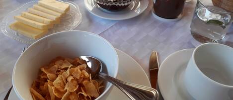 A breakfast table with cereal, butter, a muffin, a glass of juice, and a cup of coffee.