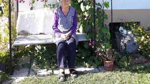Une femme est assise sur un banc, sous une structure recouverte de vignes et ornée de fleurs.