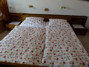 A bed with floral bedding, wooden headboard, bedside tables, and a wall-mounted light fixture. - Double room max. 2P - Greber Christine - Frühstückspension Fernblick (Schoppernau)