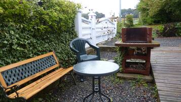 Un espace extérieur aménagé avec un banc en bois, une table en métal et un barbecue.