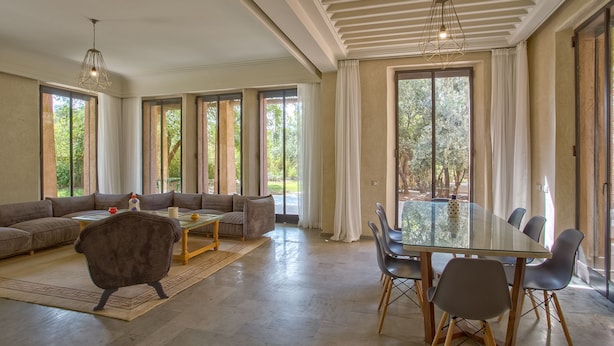 A spacious living room with a large sofa, a dining table with chairs, and a glass dining area. - Villa Touareg Domaine des Kasbahs (Marrakech)